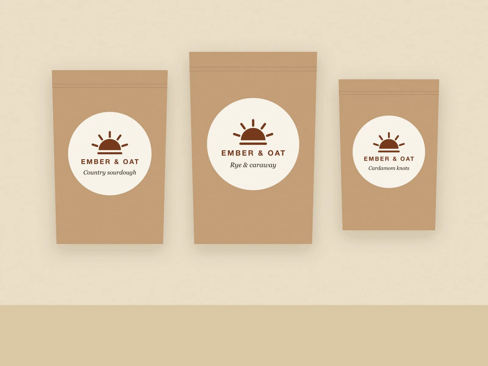 Three kraft paper bread bags with round Ember & Oat labels for country sourdough, rye and caraway, and cardamom knots